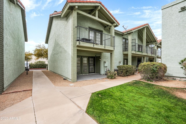 view of front of house with stucco siding, a front lawn, a tile roof, and a balcony