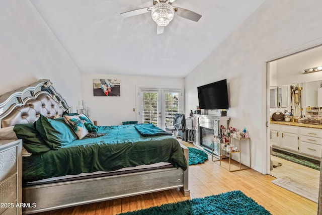 bedroom with access to exterior, vaulted ceiling, light wood-style floors, a glass covered fireplace, and ensuite bath