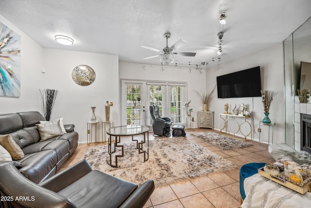 tiled living room with a tiled fireplace, track lighting, a textured ceiling, and ceiling fan