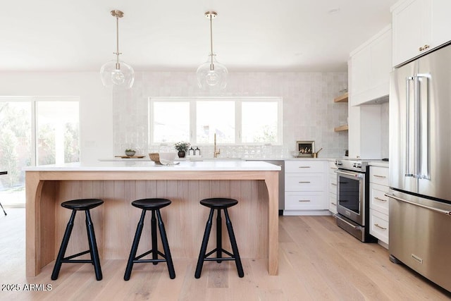 kitchen with a kitchen bar, white cabinetry, decorative light fixtures, a center island, and appliances with stainless steel finishes