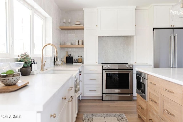 kitchen with appliances with stainless steel finishes, white cabinets, decorative backsplash, light hardwood / wood-style floors, and light brown cabinets