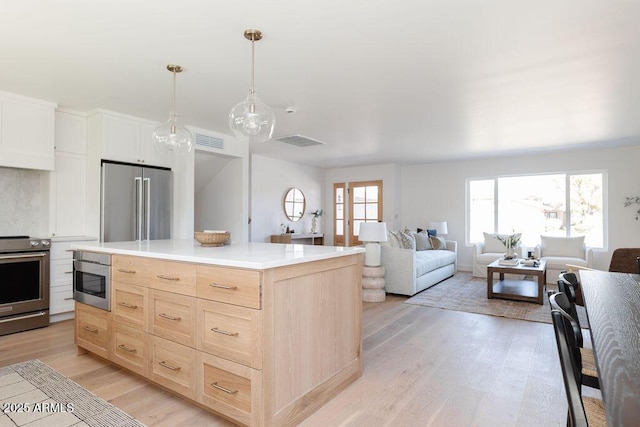 kitchen featuring light hardwood / wood-style flooring, hanging light fixtures, stainless steel appliances, a center island, and light brown cabinets