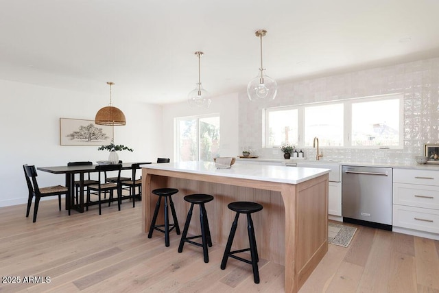 kitchen with pendant lighting, dishwasher, white cabinets, a kitchen island, and light wood-type flooring