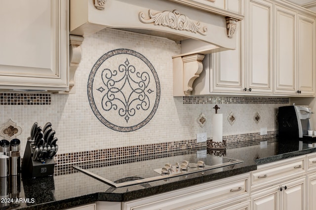 kitchen with backsplash, dark stone counters, cream cabinetry, cooktop, and custom range hood