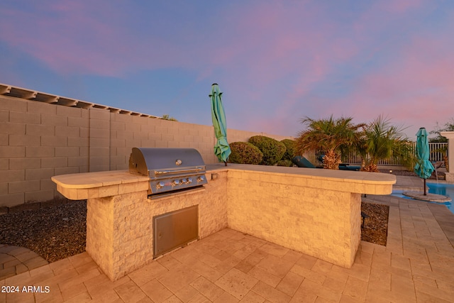 patio terrace at dusk with area for grilling and an outdoor kitchen