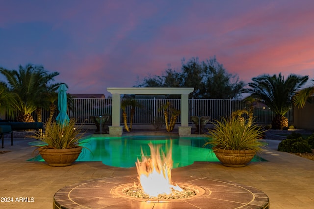 pool at dusk featuring a fire pit and a patio area