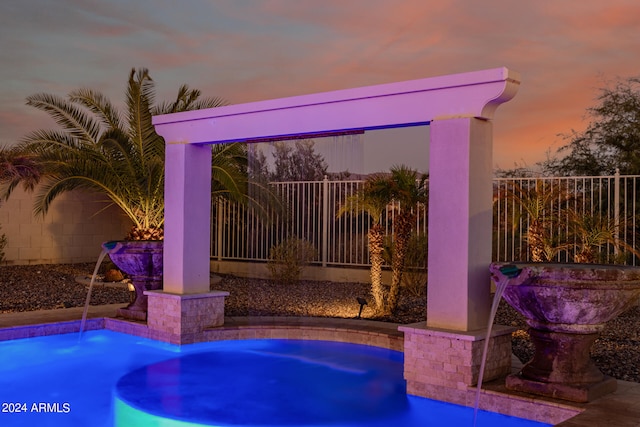 pool at dusk featuring pool water feature and a jacuzzi