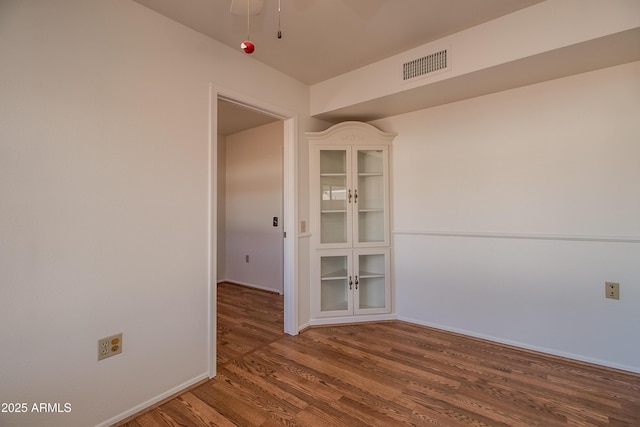 empty room with wood finished floors, visible vents, and baseboards