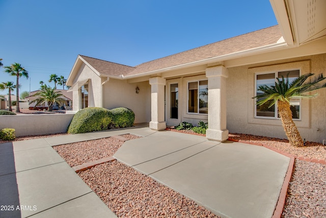 view of exterior entry featuring a shingled roof and stucco siding