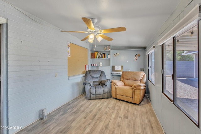 sitting room featuring light wood-style floors, a ceiling fan, vaulted ceiling, and wood walls