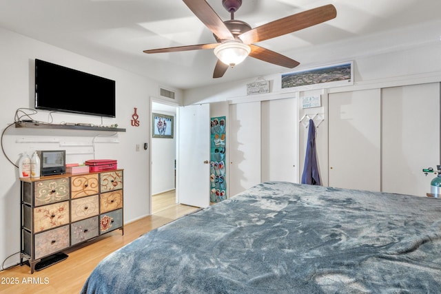 bedroom with multiple closets, a ceiling fan, wood finished floors, and visible vents