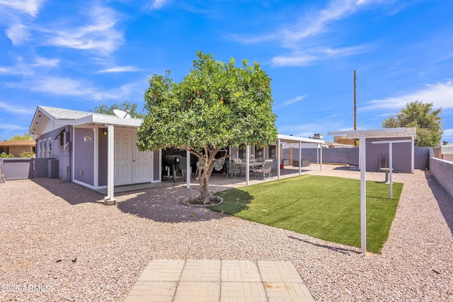 back of house with a lawn, an outbuilding, a patio area, a fenced backyard, and a storage unit