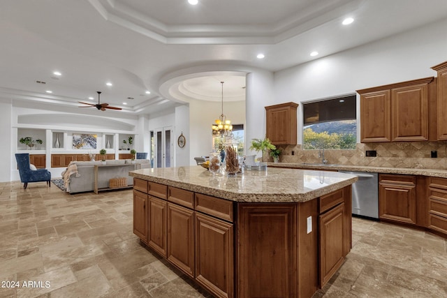 kitchen with a kitchen island, a raised ceiling, stainless steel dishwasher, ceiling fan with notable chandelier, and tasteful backsplash