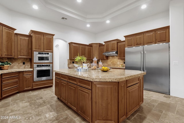 kitchen featuring appliances with stainless steel finishes, decorative backsplash, a tray ceiling, and a kitchen island