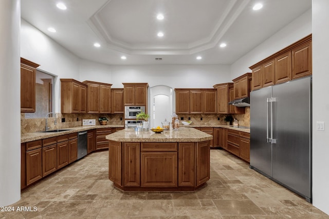 kitchen featuring a center island with sink, a raised ceiling, backsplash, sink, and stainless steel appliances