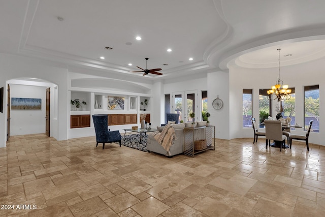 living room with ceiling fan with notable chandelier, a tray ceiling, and built in features