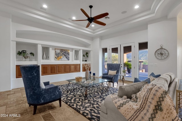 living room featuring french doors, a tray ceiling, built in features, and ceiling fan