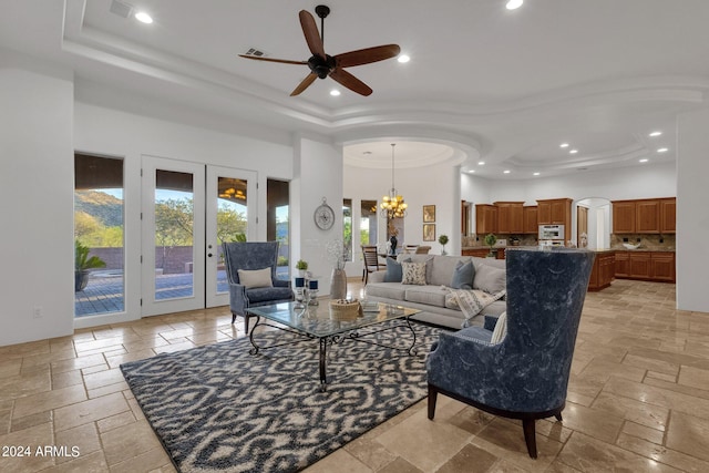 living room featuring french doors, a raised ceiling, a towering ceiling, and ceiling fan with notable chandelier