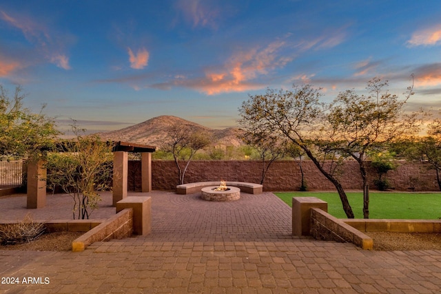 patio terrace at dusk with a mountain view, a fire pit, and a lawn