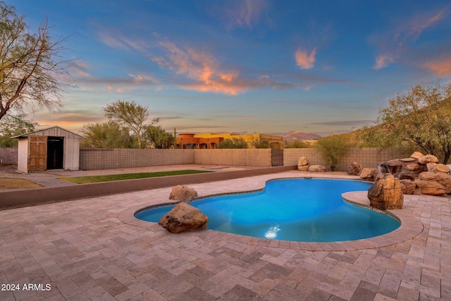 pool at dusk featuring a patio and a storage shed