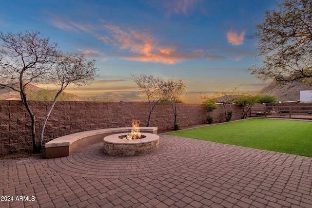 patio terrace at dusk featuring a fire pit and a yard