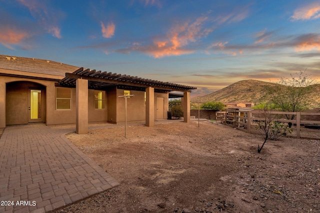 back house at dusk with a mountain view, a patio area, and a pergola