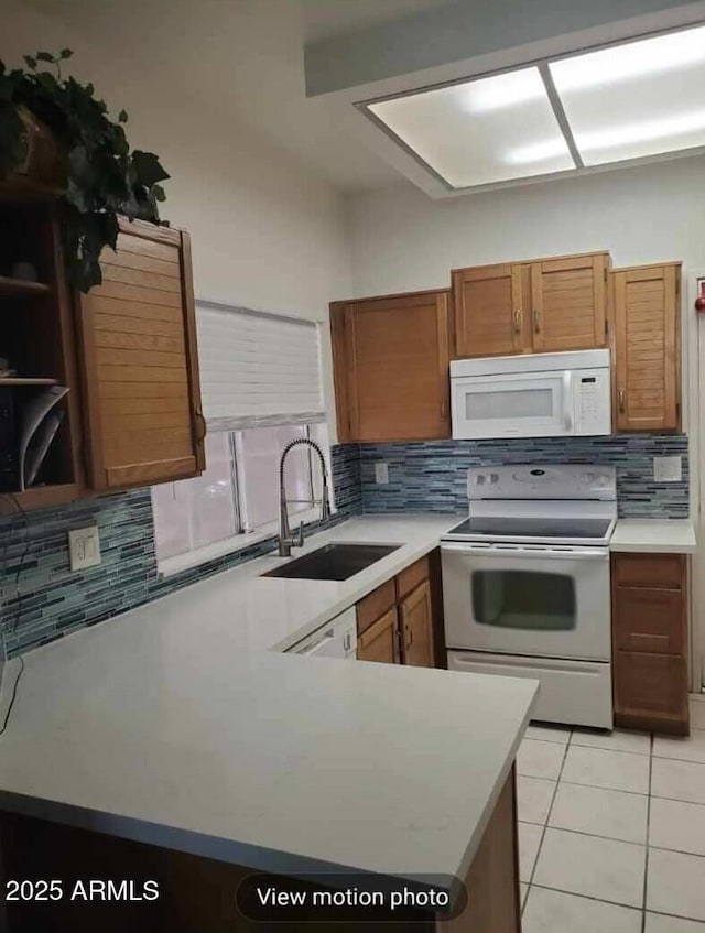 kitchen with light tile patterned flooring, white appliances, kitchen peninsula, and sink