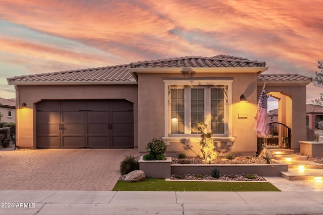 mediterranean / spanish house with decorative driveway, an attached garage, a tile roof, and stucco siding