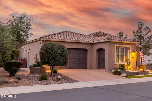 mediterranean / spanish-style house with decorative driveway, a tile roof, an attached garage, and stucco siding