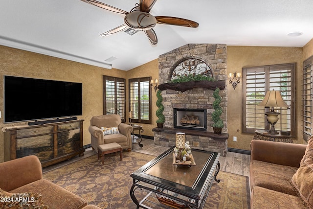 living room featuring hardwood / wood-style floors, a stone fireplace, ceiling fan, and lofted ceiling