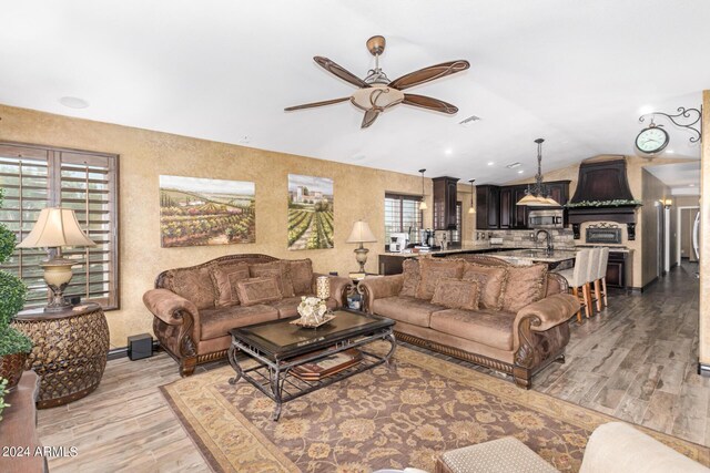 living room featuring ceiling fan, sink, vaulted ceiling, and light wood-type flooring