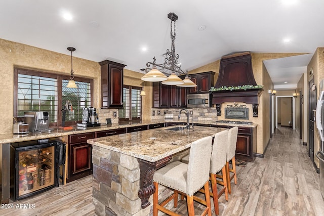 kitchen featuring dark brown cabinetry, sink, an island with sink, vaulted ceiling, and appliances with stainless steel finishes