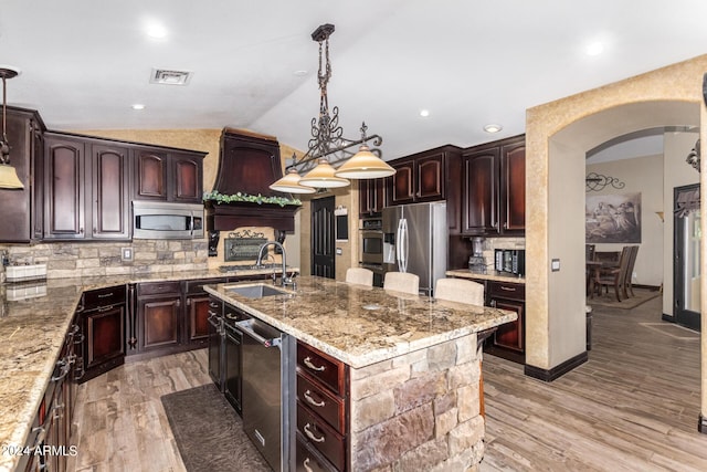 kitchen with tasteful backsplash, stainless steel appliances, vaulted ceiling, a kitchen island with sink, and hanging light fixtures