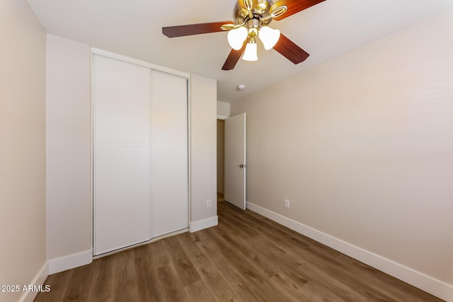 unfurnished bedroom featuring a closet, baseboards, wood finished floors, and a ceiling fan