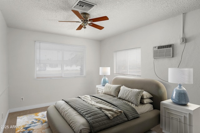 carpeted bedroom featuring a textured ceiling, visible vents, baseboards, and a wall mounted air conditioner