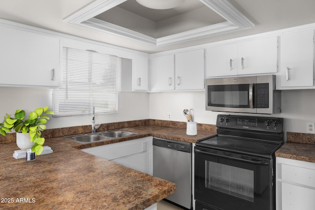 kitchen with dark countertops, a raised ceiling, white cabinets, a sink, and appliances with stainless steel finishes