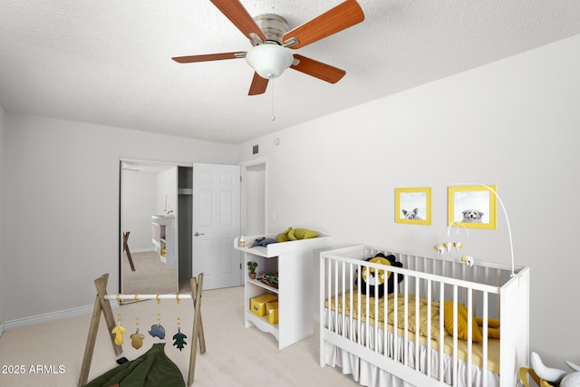 bedroom featuring a nursery area, a ceiling fan, a textured ceiling, and light colored carpet
