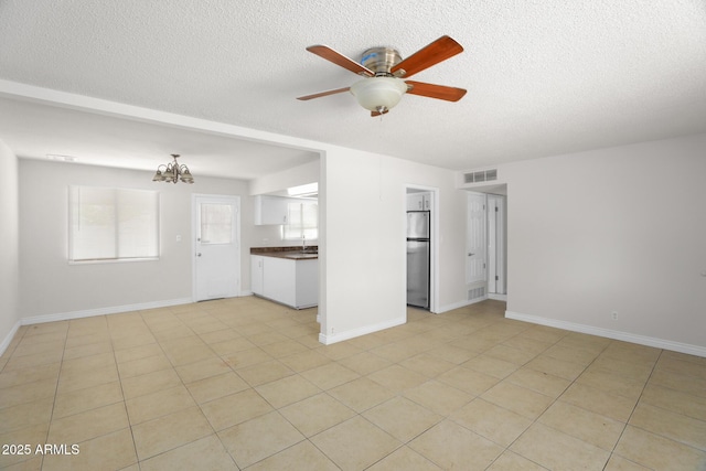 unfurnished living room featuring visible vents, a textured ceiling, ceiling fan with notable chandelier, and baseboards