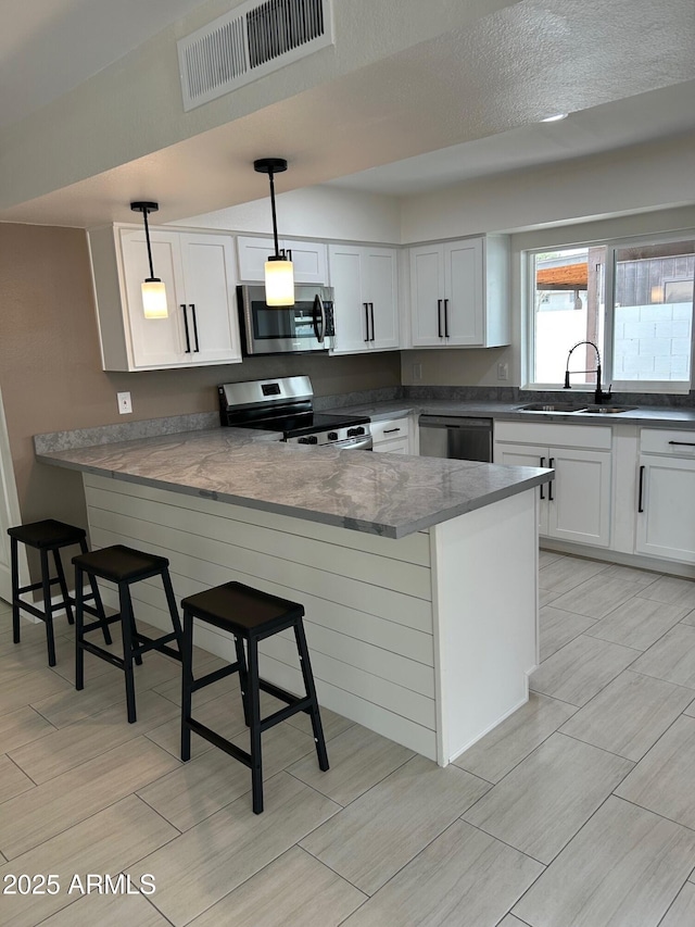 kitchen featuring sink, stainless steel appliances, a kitchen bar, decorative light fixtures, and kitchen peninsula