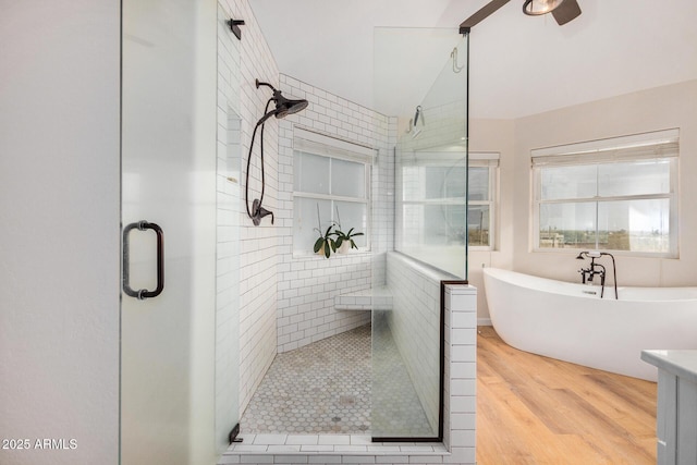 bathroom with a soaking tub, a stall shower, ceiling fan, vaulted ceiling, and wood finished floors