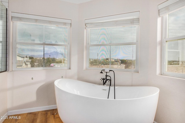 full bath featuring a wealth of natural light, a freestanding tub, baseboards, and wood finished floors