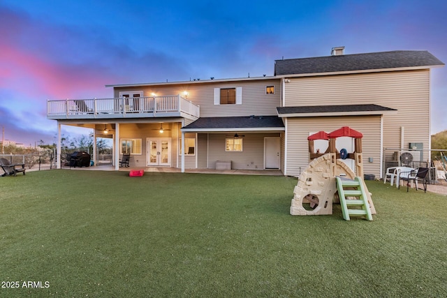 back of house at dusk with a patio, a lawn, fence, and a balcony