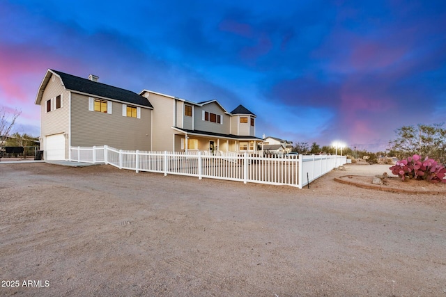 view of front of house with dirt driveway, a fenced front yard, and an attached garage