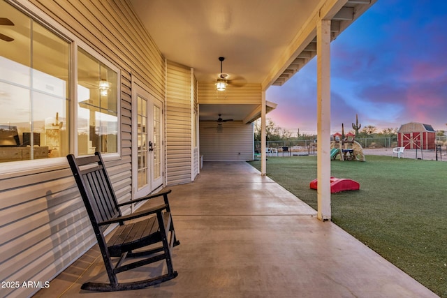 patio terrace at dusk featuring ceiling fan, fence, and a lawn