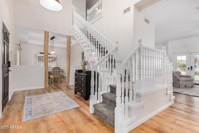 staircase with french doors, a high ceiling, wood finished floors, and visible vents