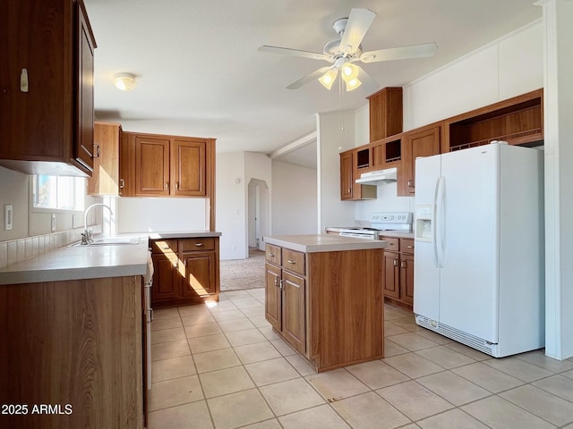 kitchen with white appliances, arched walkways, a center island, under cabinet range hood, and a sink