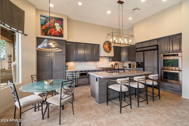 kitchen with backsplash, a high ceiling, an island with sink, dark brown cabinets, and stainless steel appliances