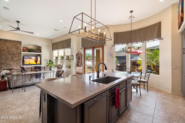 kitchen featuring built in shelves, dark brown cabinetry, sink, a kitchen island with sink, and ceiling fan with notable chandelier