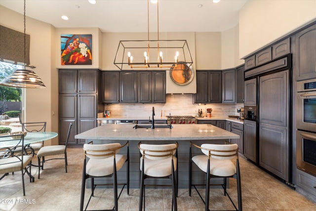 kitchen featuring decorative backsplash, dark brown cabinetry, sink, a center island with sink, and hanging light fixtures