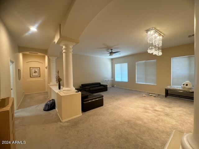 carpeted living room featuring ceiling fan with notable chandelier and ornate columns